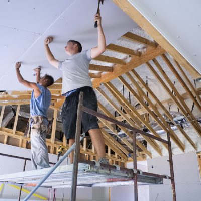 Two construction workers standing on a scaffold putting up sheetrock on a cathedral ceiling.